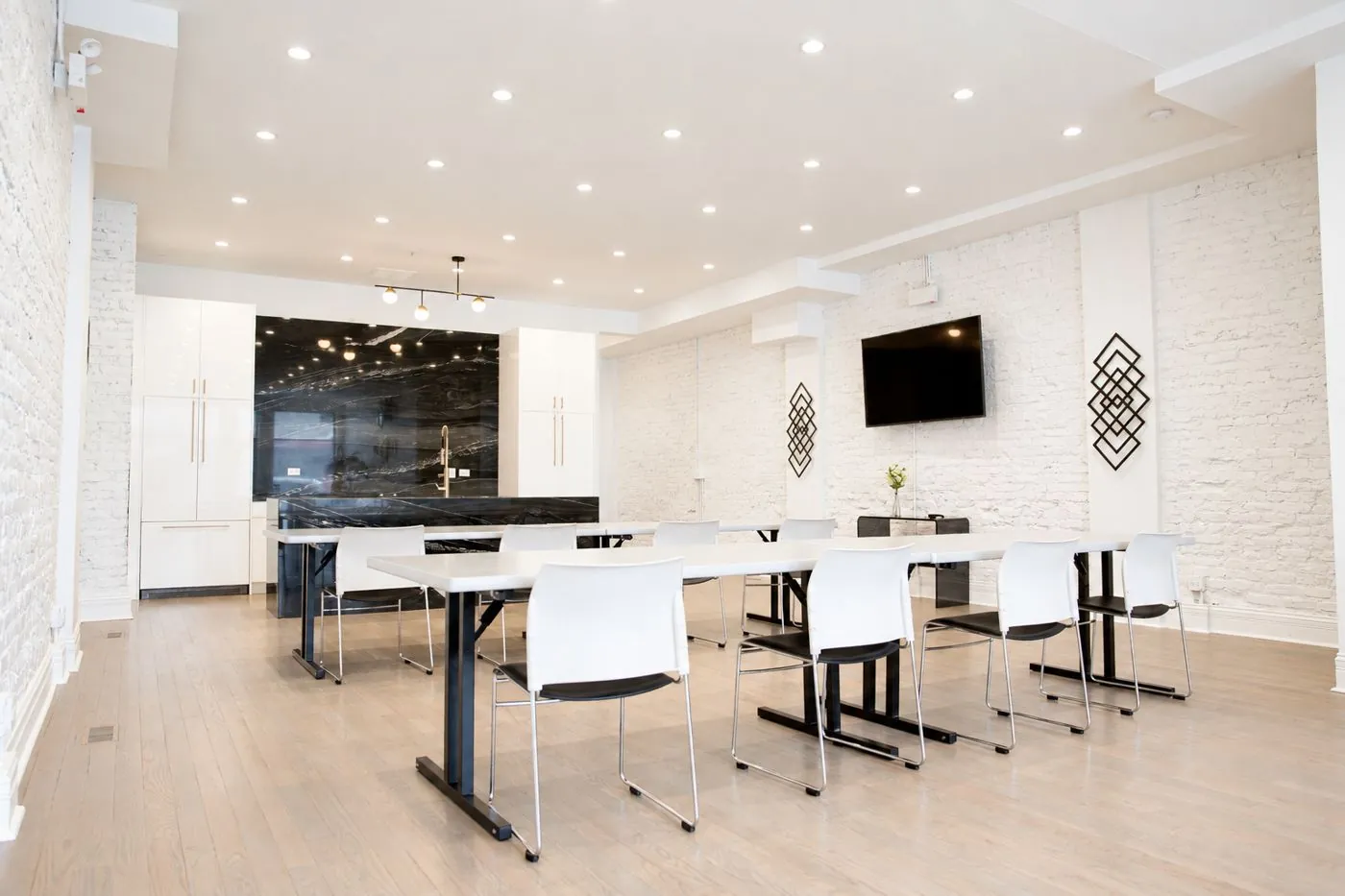 Main room at 3535 Venue set with long white tables and chairs, with the black marble kitchen island and wall-mounted TV