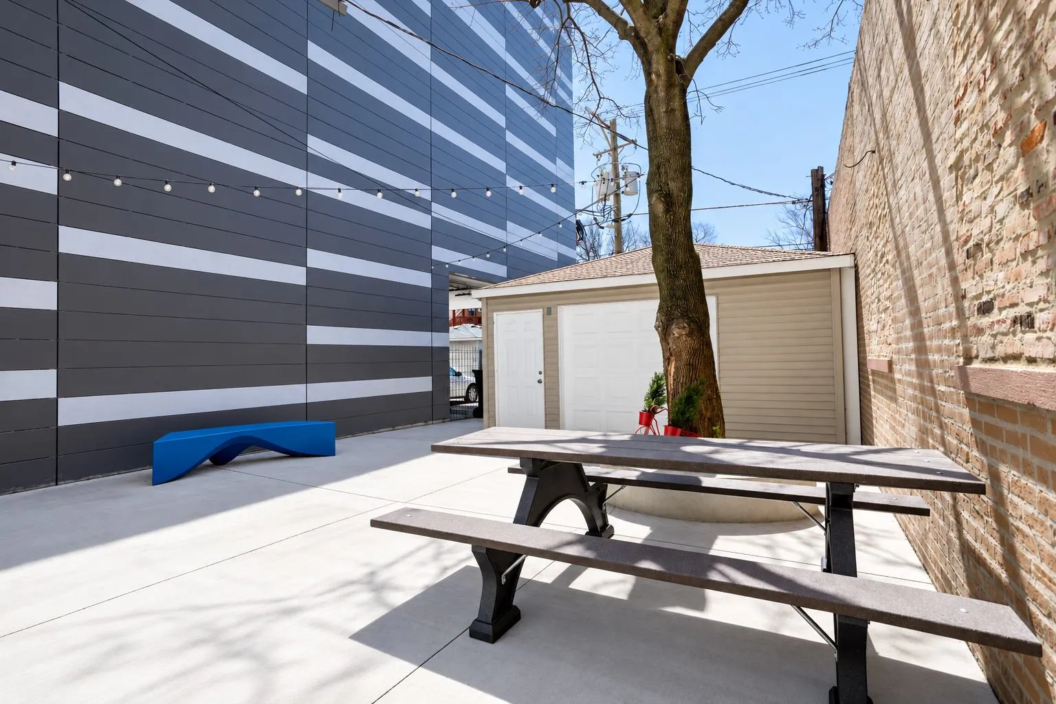 Private outdoor courtyard patio with picnic table, string lights, and blue accent bench at 3535 Venue