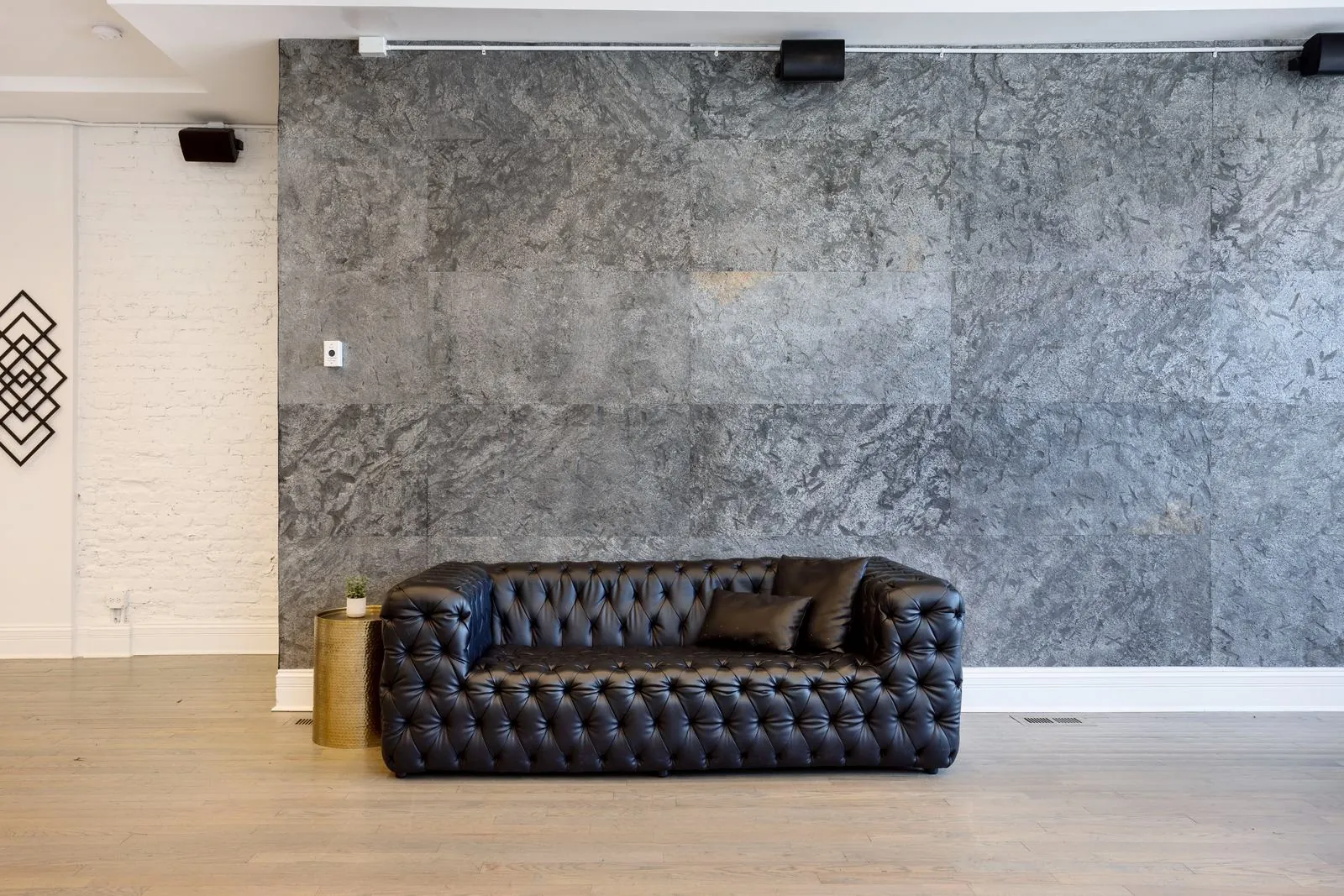 Black leather tufted sofa against a dark stone accent wall at 3535 Venue