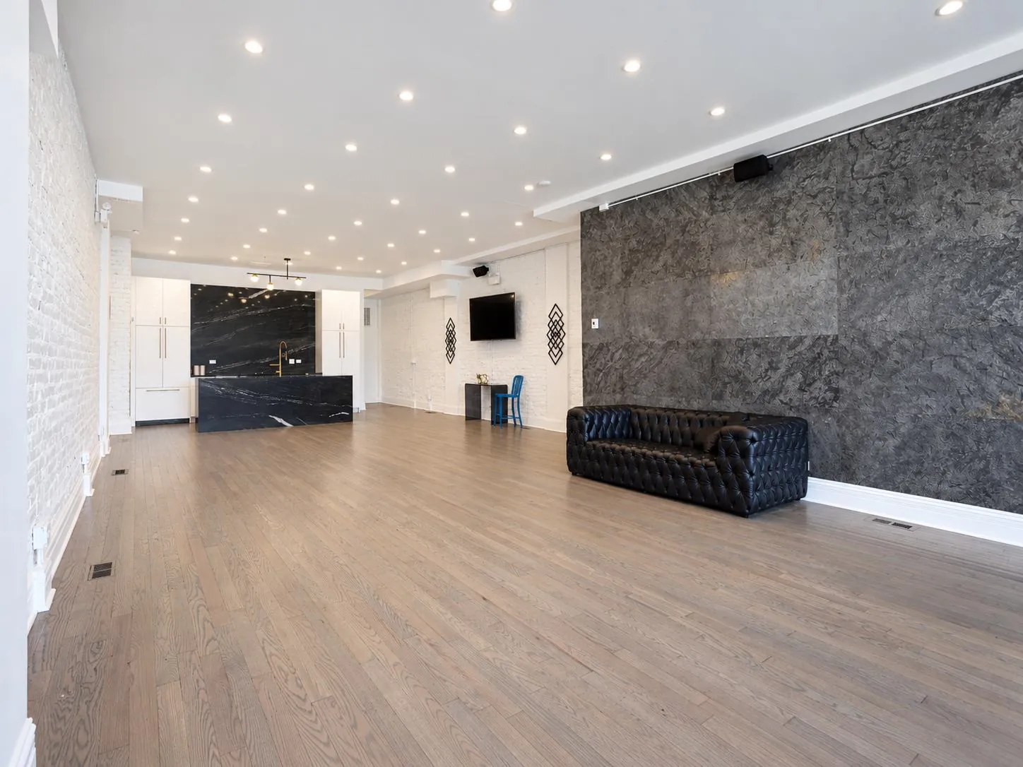 Open event space with a dark stone accent wall, black leather sofa, and kitchen in the background at 3535 Venue