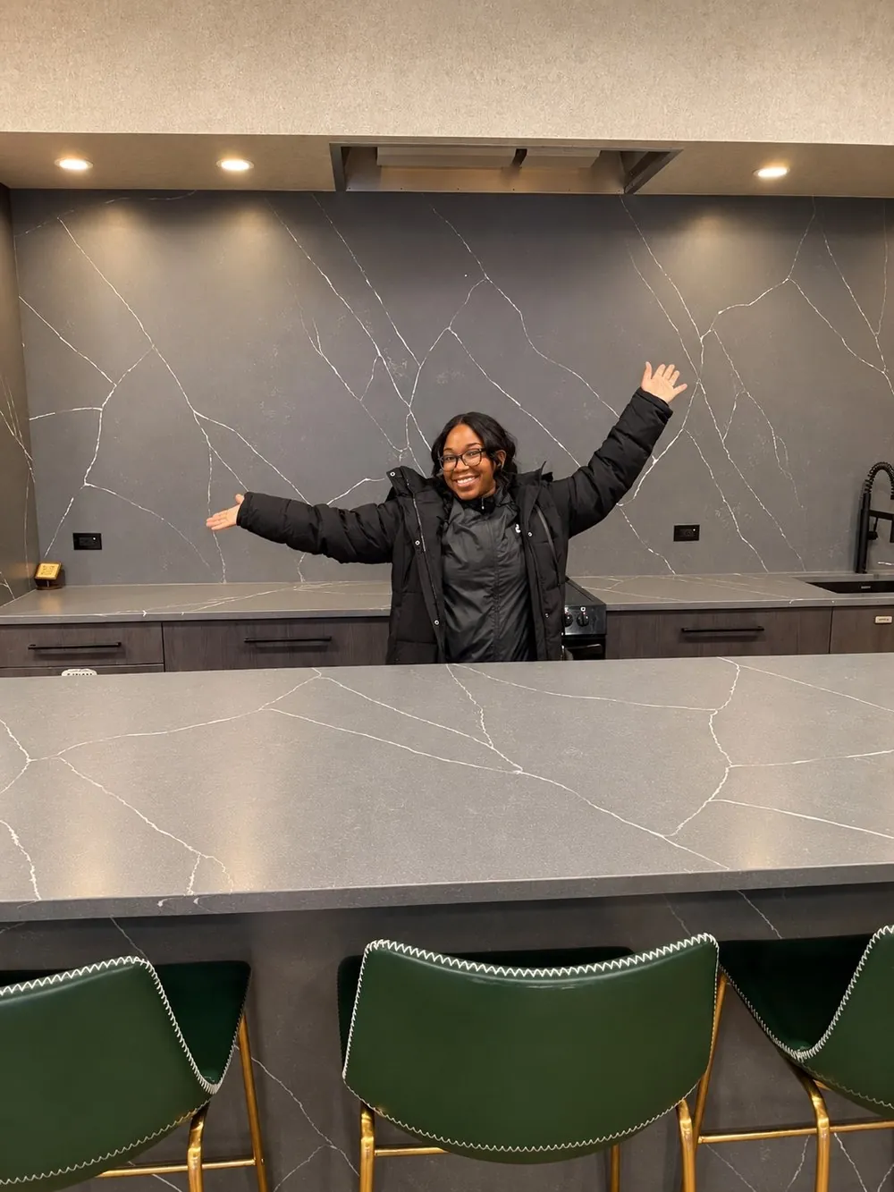 Guest behind the marble kitchen island with green leather bar stools