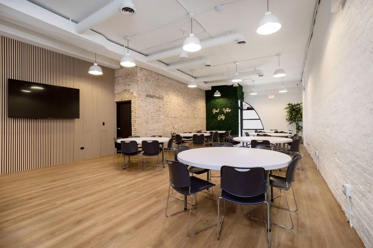 Montrose Studio main room set with round tables, a wall-mounted TV on a wood slat wall, and exposed brick