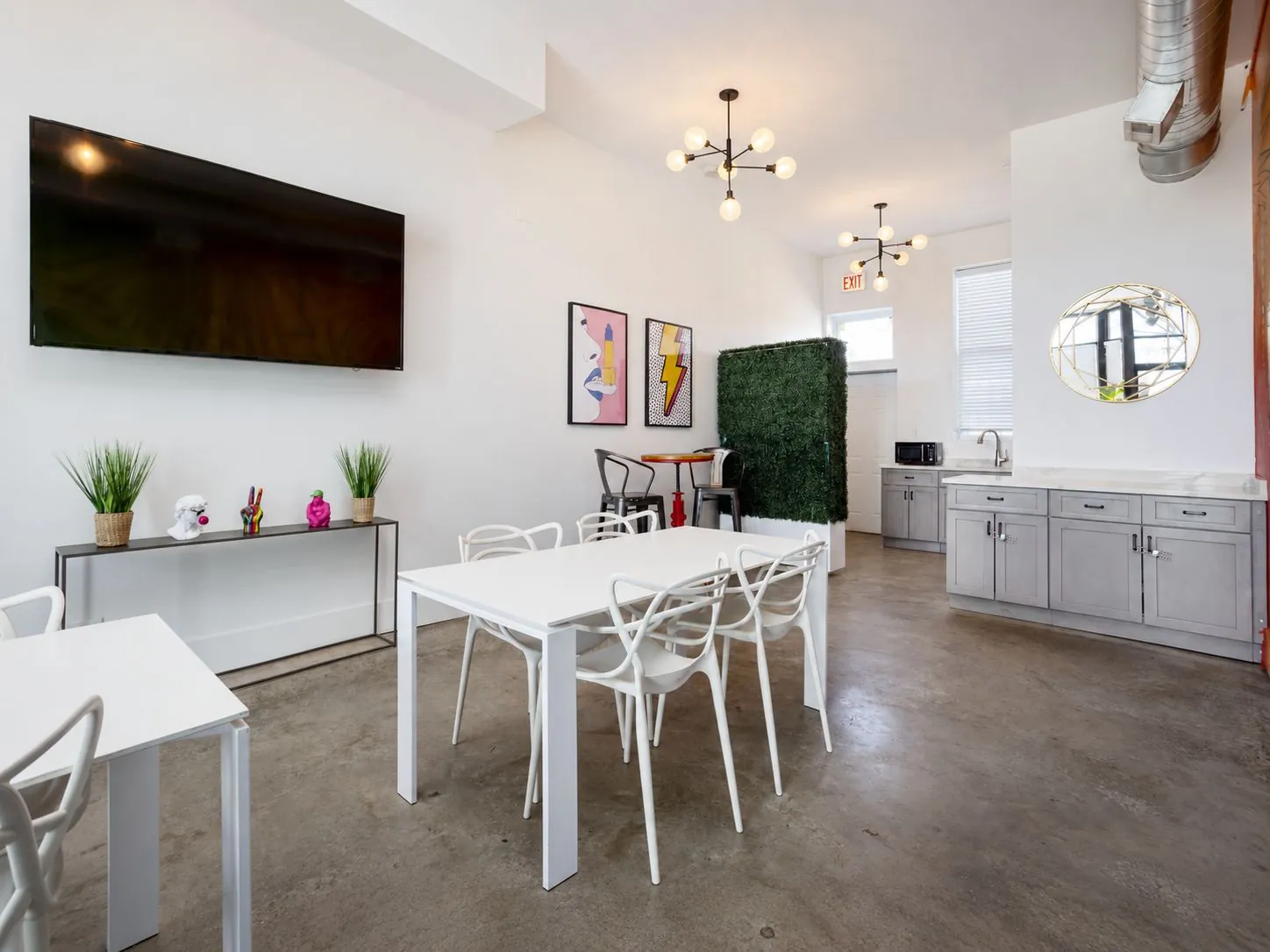 Dining tables, wall-mounted TV, bar corner, green wall, and kitchenette at Nala’s Party Room