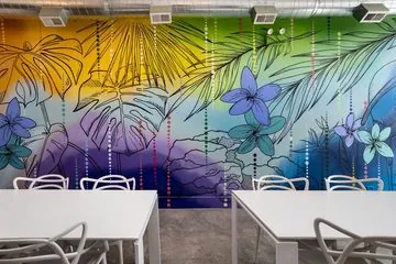 Nala’s Party Room with white tables, a tropical mural and a wall-mounted TV