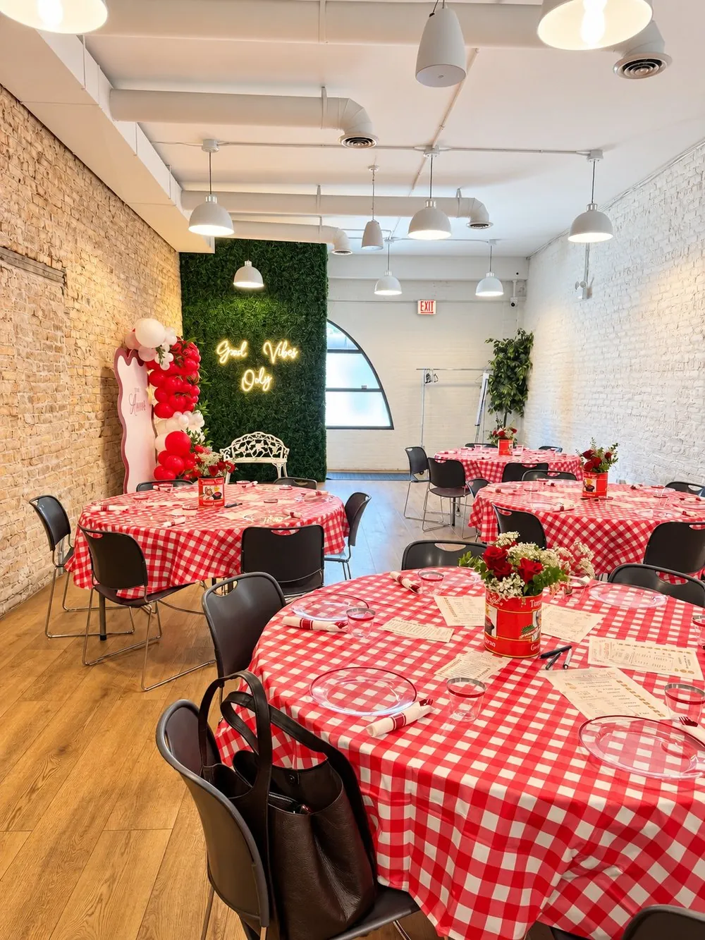 Round tables with red gingham tablecloths, a balloon arch and the green wall with a neon sign at a bridal shower